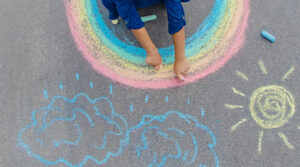kids drawing a rainbow sun and rain clouds with chalk