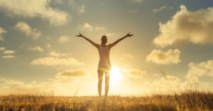 person with their arms up facing the sun outside in a field