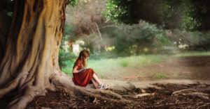 child writing and sitting on tree roots outside